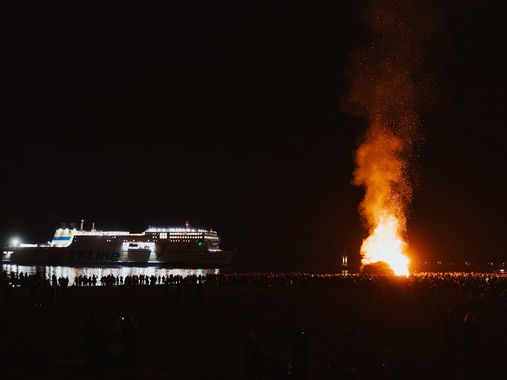  Das Osterfeuer am Strand von Travemünde. Im Hintergrund fährt ein Schiff der TT-Line in den Hafen ein.