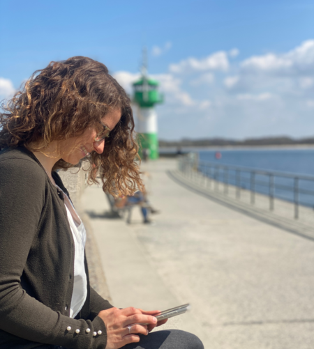 Eine Frau schaut an der Travemünder Nordermole auf ihr Handy.