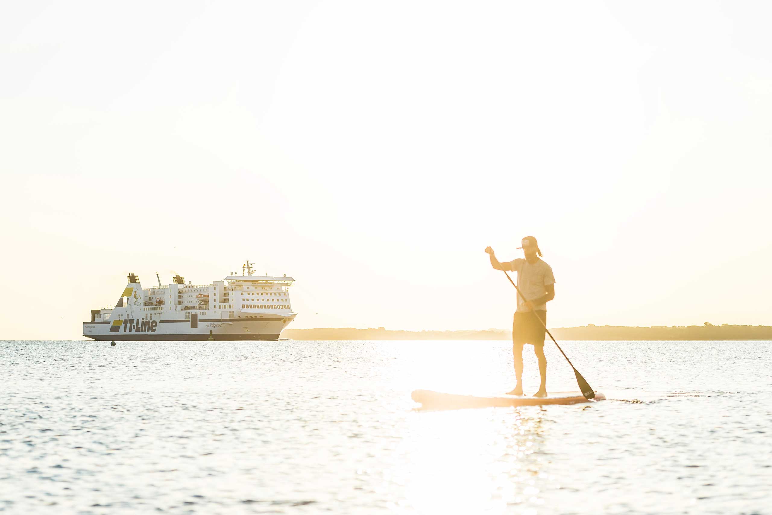 Mann mit SUP Board auf dem Wasser, im Hintergrund die TT-Line