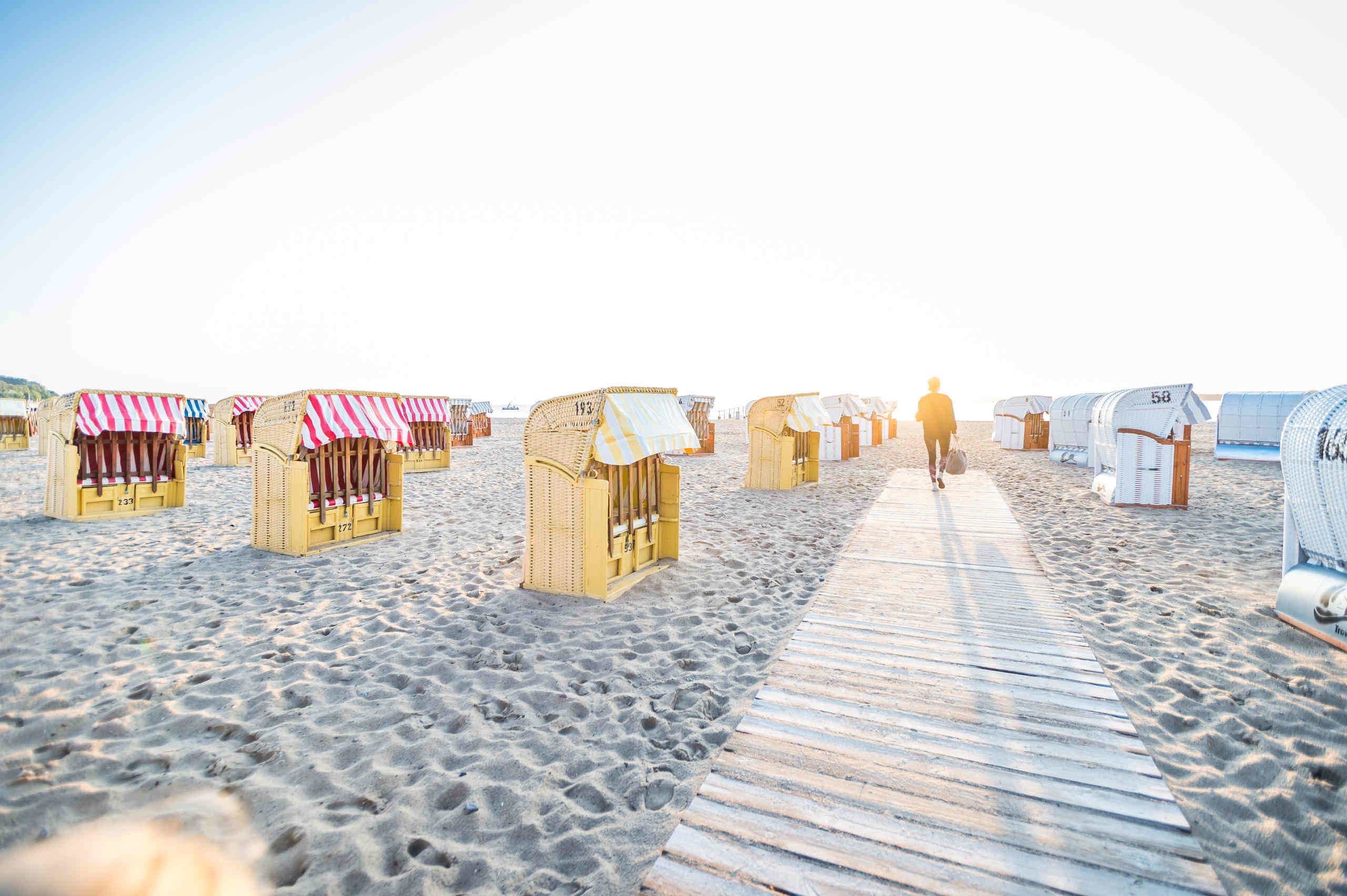 Frau spaziert am Travemünder Strand zwischen Strandkörben entlang