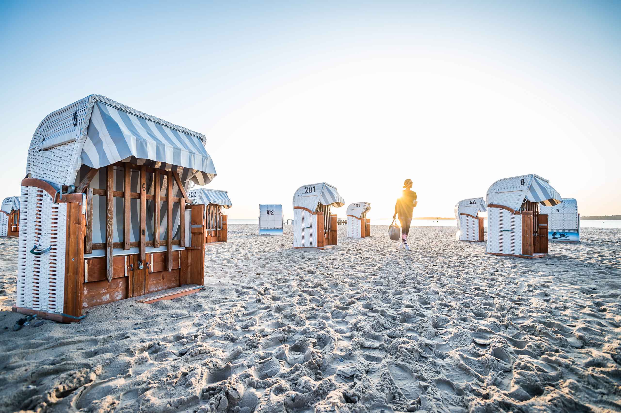 Strandkörbe und eine Frau bei Sonnenuntergang am Strand