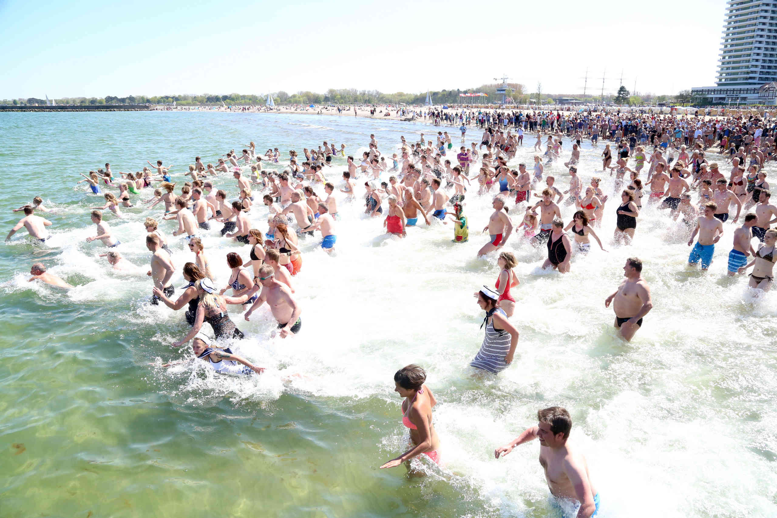 Große Personengruppe läuft und springt ins Wasser 